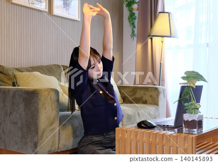A woman refreshes herself with stretches during a break from remote work. A woman refreshes herself with stretches during a break from remote work. 140145893