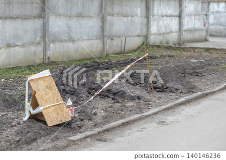 Orange and white caution tape barrier surrounding a muddy patch of ground near a concrete wall, representing restricted access or an ongoing urban infrastructure development site Orange and white caution tape barrier surrounding a muddy patch of ground near a concrete wall, representing restricted access or an ongoing urban infrastructure development site 140146236