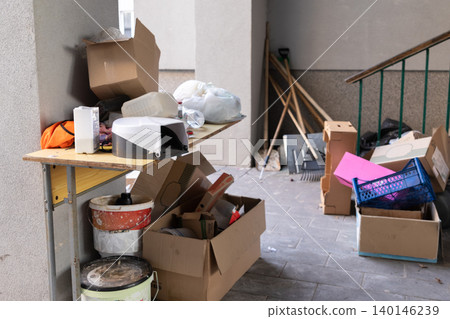 Discarded cardboard boxes and household clutter on a wooden desk inside a dark building hallway, capturing a scene of mess, disorganized storage, and domestic waste management issues Discarded cardboard boxes and household clutter on a wooden desk inside a dark building hallway, capturing a scene of mess, disorganized storage, and domestic waste management issues 140146239