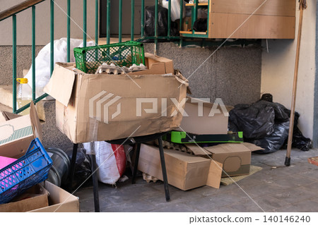 Stacked cardboard boxes and plastic crates piled on a small table outside an urban apartment, representing domestic waste management, recycling preparation, and cluttered living 140146240