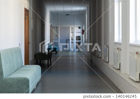 A long empty office hallway with pastel blue soft benches and white walls creates a clean professional atmosphere for a modern corporate environment or a quiet medical waiting area A long empty office hallway with pastel blue soft benches and white walls creates a clean professional atmosphere for a modern corporate environment or a quiet medical waiting area 140146245