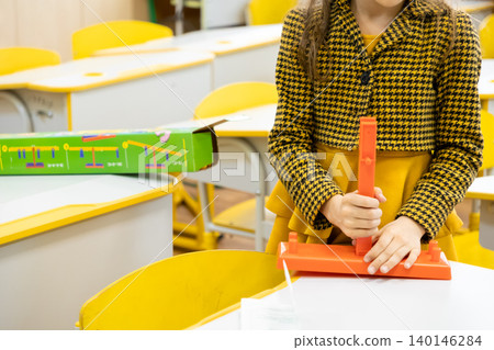 A young student assembles a plastic balance scale on a classroom desk to highlight interactive STEM education tools and hands-on learning methods in a modern school environment A young student assembles a plastic balance scale on a classroom desk to highlight interactive STEM education tools and hands-on learning methods in a modern school environment 140146284