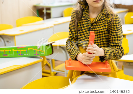 A young schoolgirl builds with plastic mathematical balance scales in a colorful classroom, representing early childhood education, interactive learning, and logic skill development A young schoolgirl builds with plastic mathematical balance scales in a colorful classroom, representing early childhood education, interactive learning, and logic skill development 140146285