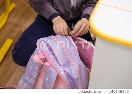 A young student opens a vibrant purple backpack inside a classroom to show school preparation and organization for a productive day of academic study with a cheerful accessory A young student opens a vibrant purple backpack inside a classroom to show school preparation and organization for a productive day of academic study with a cheerful accessory 140146293