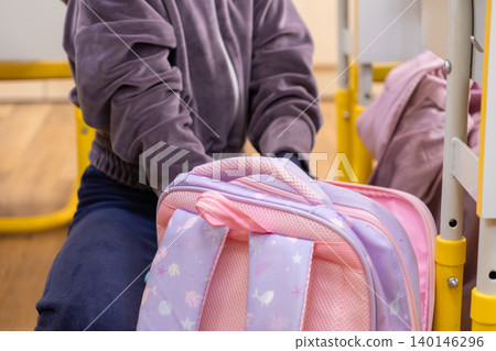 A young student diligently packs a colorful school bag while sitting at a wooden classroom desk, highlighting academic preparation and the daily routine of a child in school A young student diligently packs a colorful school bag while sitting at a wooden classroom desk, highlighting academic preparation and the daily routine of a child in school 140146296