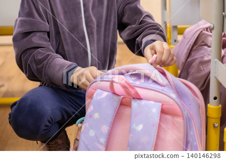 A young child kneels to open a colorful school backpack in a bright classroom, reflecting daily preparation for primary education and the excitement of learning in a school routine A young child kneels to open a colorful school backpack in a bright classroom, reflecting daily preparation for primary education and the excitement of learning in a school routine 140146298