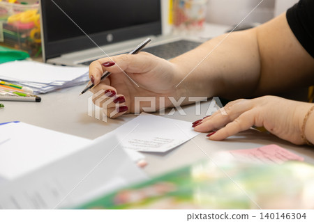 A professional person writes with a pen on a small white note at an office desk with a laptop, conveying meticulous organization, daily business planning, and administrative focus A professional person writes with a pen on a small white note at an office desk with a laptop, conveying meticulous organization, daily business planning, and administrative focus 140146304