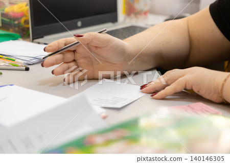 Person holding a metal ballpoint pen over paper at a desk, capturing a professional moment of planning or creative task management in a brightly lit, organized modern office space 140146305