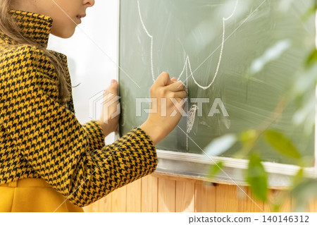 School girl writing with white chalk on a green classroom blackboard, representing the joy of early childhood education and the creative learning process in a bright academic setting School girl writing with white chalk on a green classroom blackboard, representing the joy of early childhood education and the creative learning process in a bright academic setting 140146312