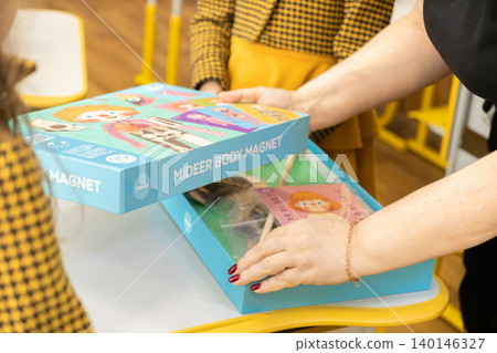 A teacher opens an educational human anatomy magnet puzzle box in a bright classroom to show interactive learning tools for biology lessons and cognitive child development training A teacher opens an educational human anatomy magnet puzzle box in a bright classroom to show interactive learning tools for biology lessons and cognitive child development training 140146327