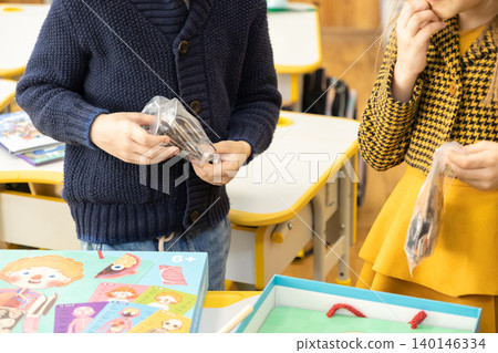 Two young children hold plastic bags with game pieces at a school desk while playing a creative biology board game to foster a deep interest in science during a modern lesson Two young children hold plastic bags with game pieces at a school desk while playing a creative biology board game to foster a deep interest in science during a modern lesson 140146334