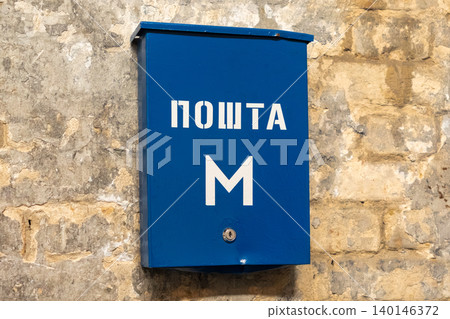 Blue metal mailbox mounted on a textured stone wall in an outdoor urban setting, symbolizing local postal communication and historical city architecture within a classic street scene Blue metal mailbox mounted on a textured stone wall in an outdoor urban setting, symbolizing local postal communication and historical city architecture within a classic street scene 140146372