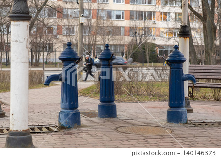 Three blue vintage cast iron water pumps stand along a paved city walkway, reflecting a historic urban design element in a contemporary residential neighborhood during autumn Three blue vintage cast iron water pumps stand along a paved city walkway, reflecting a historic urban design element in a contemporary residential neighborhood during autumn 140146373