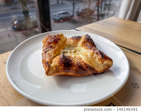 Fresh savory puff pastry with sesame seeds on a white plate at a cafe table, illustrating a delicious golden baked breakfast snack for a cozy morning meal in an urban atmosphere 140146391