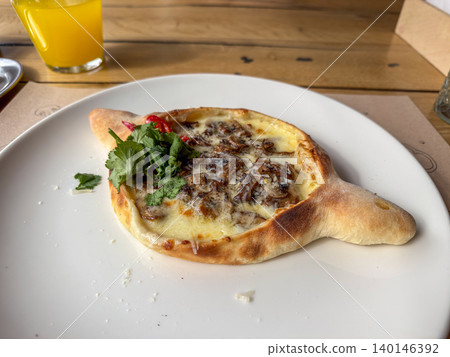 Freshly baked mushroom khachapuri served on a white plate with orange juice, embodying authentic Georgian cuisine and traditional culinary craftsmanship in a warm rustic restaurant Freshly baked mushroom khachapuri served on a white plate with orange juice, embodying authentic Georgian cuisine and traditional culinary craftsmanship in a warm rustic restaurant 140146392