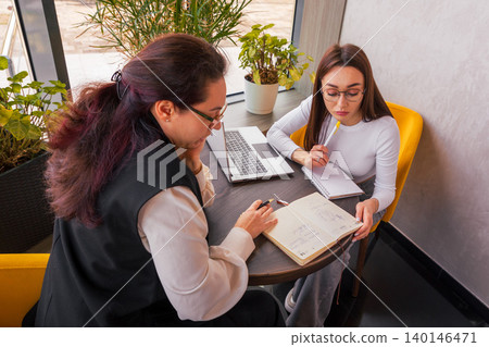 Enthusiastic brainstorming session between young women discussing outreach strategy. Business planning at a cozy cafe. Concept of creative entrepreneurship. 140146471