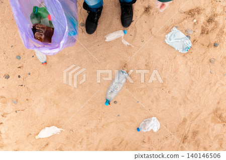 Person stands on a sandy beach with trash bag. Copy space. Top view. The concept of environmental protection and Earth Day Person stands on a sandy beach with trash bag. Copy space. Top view. The concept of environmental protection and Earth Day 140146506