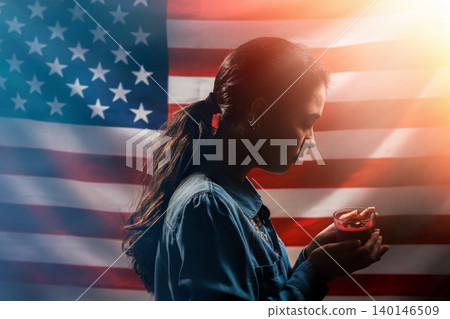 Memorial day. A woman holds a candle in memory of the victims. In the background, the American flag. Side view. Light. Concept of American holidays Memorial day. A woman holds a candle in memory of the victims. In the background, the American flag. Side view. Light. Concept of American holidays 140146509