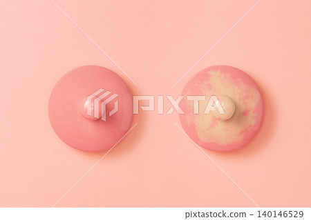 Two pink ceramic lids on a pink background symbolizing the female breast. Right side lid dirtied. Flat lay. Copy space. Concept of Breast Cancer Awareness Month Two pink ceramic lids on a pink background symbolizing the female breast. Right side lid dirtied. Flat lay. Copy space. Concept of Breast Cancer Awareness Month 140146529