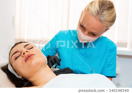 Plastic surgery at cosmetology salon. Doctor in gloves and protective mask makes a syringe injects to the female client. Lifting and aesthetic medicine 140146540