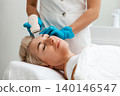 Professional care. A cosmetologist in blue gloves does an ultrasound cleaning of a woman's face. Cleansing and rejuvenating procedure in a beauty salon. Side view 140146547
