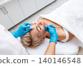 Professional skin care in beauty salon. Cosmetologist does a deep mechanical cleaning with spatula of the client's face. View from the shoulders 140146548