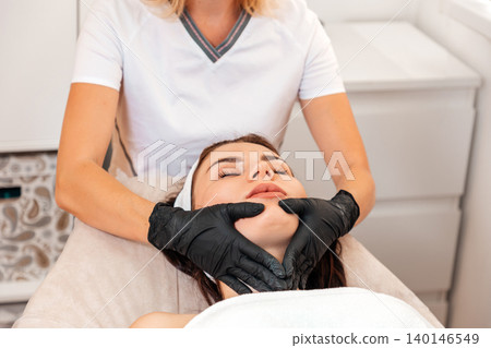 Spa and beauty procedure. Professional cosmetologist gives a facial massage to the client in salon. Close up. Concept of cosmetology and lifting 140146549