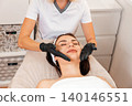 Professional cosmetologist gives a facial massage to the client in salon. Close up. Top view. Concept of Spa and beauty procedures 140146551