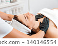 Concept of lifting and beauty procedures. Professional cosmetologist gives a facial massage to the client in salon. Close up. View from the shoulders. Spa and rejuvenation 140146554