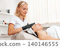Lifting therapy. Professional beautician gives a rejuvenation facial massage to the client in salon. Concept of cosmetology 140146555