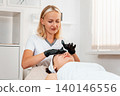 Cosmetology and lifting. Professional beautician in latex gloves gives a facial massage to the client in salon. Concept of beauty procedures 140146556