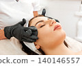 Cosmetology and beauty procedures. Professional beautician gives a facial massage with jade stones to the client in salon. Close up of female face. Concept of rejuvenation 140146557