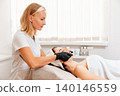 Professional beautician in protective gloves gives a rejuvenation facial massage to the client in salon. Concept of cosmetology and beauty procedure 140146559