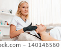 Cosmetology and lifting. Professional beautician gives a facial massage to the client in salon. Concept of rejuvenation and beauty procedures 140146560