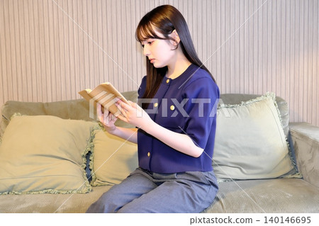 A blissful indoor holiday. Enjoying a book while bathed in soft light—a sophisticated adult relaxation time. A blissful indoor holiday. Enjoying a book while bathed in soft light—a sophisticated adult relaxation time. 140146695