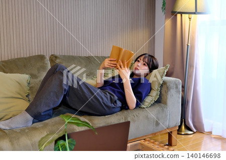 A blissful indoor holiday. Enjoying a book while bathed in soft light—a sophisticated adult relaxation time. A blissful indoor holiday. Enjoying a book while bathed in soft light—a sophisticated adult relaxation time. 140146698