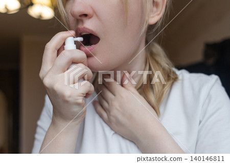 Blonde woman using throat spray to relieve pain. Close up of female treating sore throat or seasonal illness with medication at home. 140146811