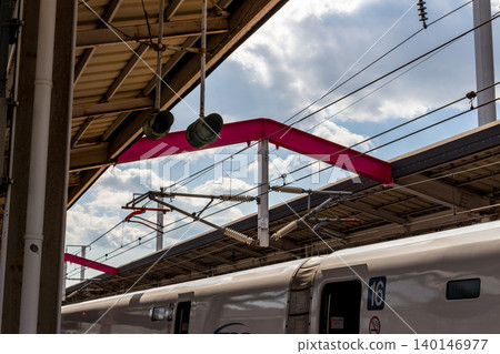 A Shinkansen train stopped at the platform of Okayama Station on the Sanyo Shinkansen line, with its distinctive pink beams [overhead line equipment]. 140146977
