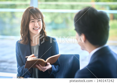 A Japanese businesswoman smiles as she conducts business negotiations, holding her notebook. A Japanese businesswoman smiles as she conducts business negotiations, holding her notebook. 140147242