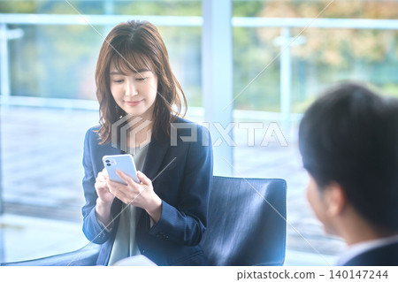 一位日本女性一邊展示智慧型手機螢幕一邊處理公務。 一位日本女性一邊展示智慧型手機螢幕一邊處理公務。 140147244