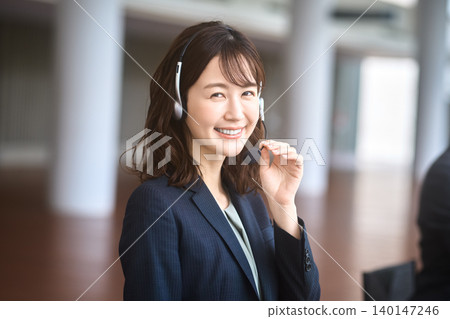一位日本女性在呼叫中心工作,戴著耳機,微笑著接聽電話。 一位日本女性在呼叫中心工作,戴著耳機,微笑著接聽電話。 140147246