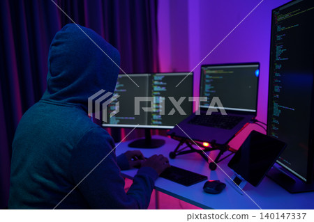Hacker Coding at Multi-Monitor Desk in Dark Neon Room 140147337