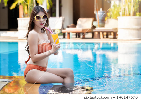 Sexy young asian woman in swimsuits in summer. beautiful woman in orange bikini with sunglasses and tropical drink sitting in swimming pool. 140147570