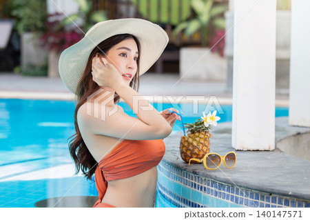 Sexy young asian woman in swimsuits in summer. beautiful woman in orange bikini with hat and tropical drink in swimming pool. Sexy young asian woman in swimsuits in summer. beautiful woman in orange bikini with hat and tropical drink in swimming pool. 140147571