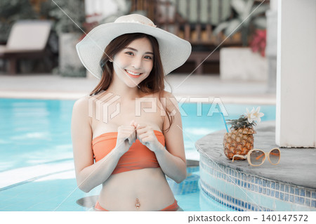 Sexy young asian woman in swimsuits in summer. beautiful woman in orange bikini with hat and tropical drink in swimming pool. 140147572
