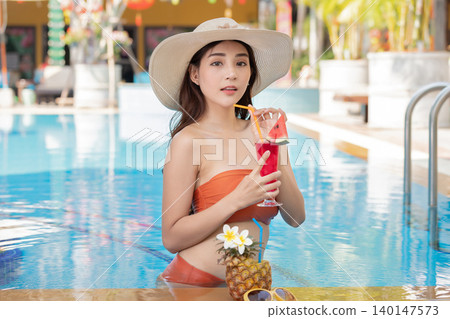 Sexy young asian woman in swimsuits in summer. beautiful woman in orange bikini with tropical drink in swimming pool. 140147573