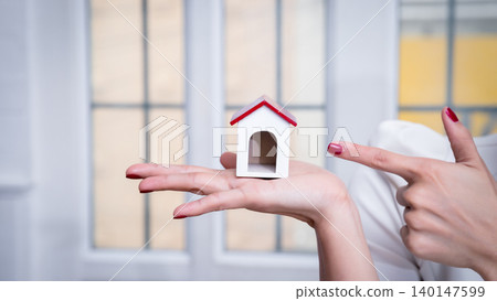 Business, architecture, building construction and real estate concept. Female real estate agent presenting a house model. Young female architect holding model of house in office. Business, architecture, building construction and real estate concept. Female real estate agent presenting a house model. Young female architect holding model of house in office. 140147599