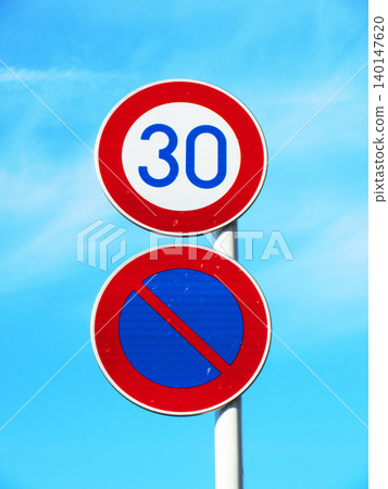 A road sign indicating a maximum speed limit of "30 km/h" and "no parking" against a backdrop of a blue sky. 140147620