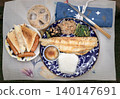 A blue patterned plate holds a grilled fish fillet, white rice, grated radish, and three sides: hijiki seaweed, simmered roots, and greens. To the left, a smaller plate has toast triangles and three 140147691