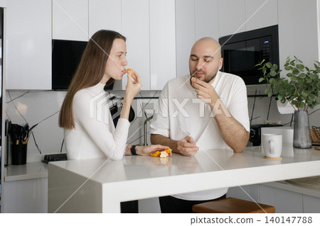 Attractive couple eating fruit and drinking coffee in domestic kitchen at home 140147788